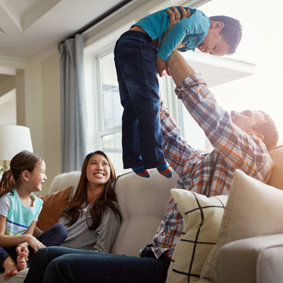 Father lifting small son skyward as he sits on the couch with smiling mother and daughter Father lifting small son skyward as he sits on the couch with smiling mother and daughter