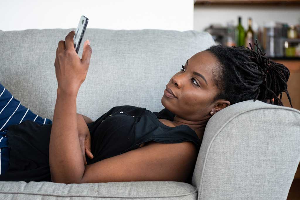 Picture of a lady using a mobile phone while laying on the couch.