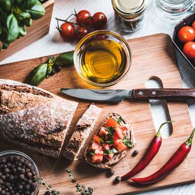 Sliced rustic bread on cutting board with oil and vegetables Sliced rustic bread on cutting board with oil and vegetables