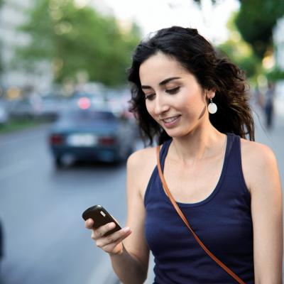 Young woman walking along city sidewalk and checking her smartphone