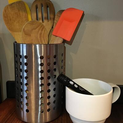 Accu-Chek FastClix device sitting in empty white coffee mug on kitchen counter next to utensils bin