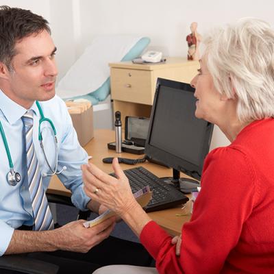 Young male physician at his computer desk discussing treatment with elderly female patient