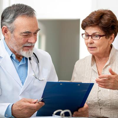 Elderly physician holding clipboard and discussing results with female patient