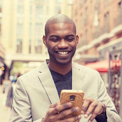 Smiling man using smartphone while walking down a crowded urban sidewalk