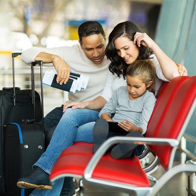 Mother, father, and daughter waiting in airport terminal with passports in hand and suitcases by the side
